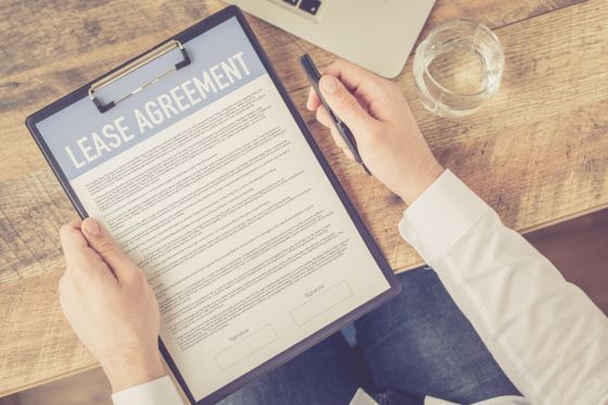 Lease agreement on a clipboard held by a man. A glass of water is nearby.