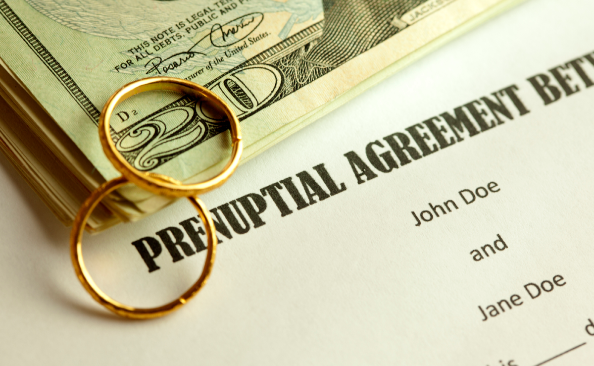Wedding rings and paper money sitting on top of a Prenuptial Agreement legal document.