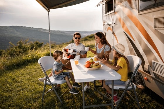 A family enjoying food and playing guitar outside of their camper